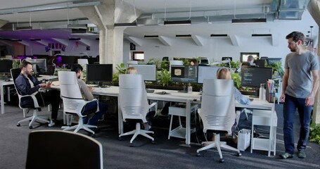Rear of people developers sitting at computers and working. Back view on support office employees. Man coming and helping in IT work to woman colleague. Male and female talking and discussing.