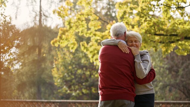 European elderly gray-haired retired couple embracing each other after spontaneous dance in the park. Autumn vibes. High quality photo