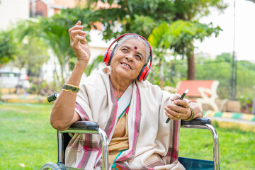 Enjoying senior woman with disability listening songs on mobile phone with headphones while sitting...