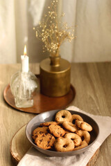 Bowl of sugar cookies and chocolate chip cookies, lit candle and vase with flowers on the table. Selective focus.