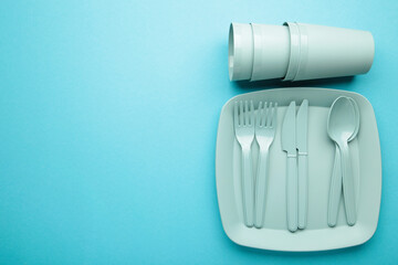 Bright plastic disposable tableware on blue background. Space for text