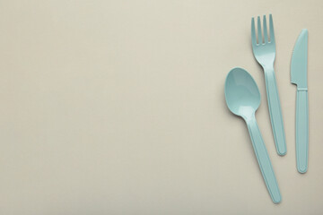 Many blue plasic forks, spoons and knives on grey background with copy space, top view.