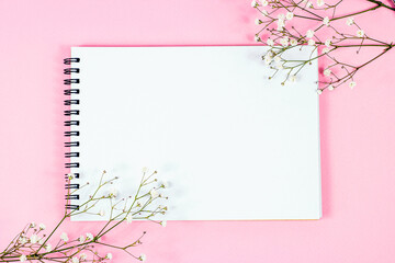 Whate blank notebook page with copy space for text with little flowers on pastel pink background top view. Empty wedding paper mockup, romantic Valentine letter template.