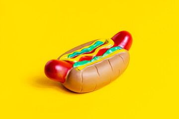 Toy American rubber hot dog with sausage, bun and mustard on bright yellow background.