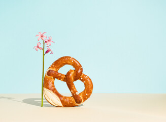Bread bagel in heart shape with sesame seeds and pink hyacinth on sky blue background. Minimal food concept. Traditional Turkish pastry food.