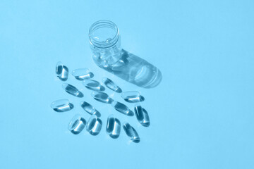 Pills and glass pill bottle on blue background. Big golden tablets. Omega 3 capsules. Close up, top view. Health care concept. Healthy every day fatty acids nutritional supplement dosage. Flat lay