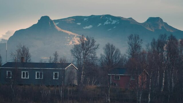 Small cabins in rural scandinavia. Snow-capped mountains tower in the backgrouns. Slow-motion. pan follow.