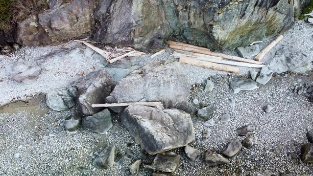 Aerial footage of a rocky beach. Pulling back to reveal cliff, ocean, and a wider beach