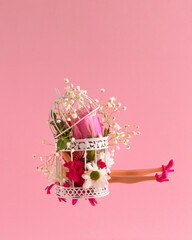 Woman legs and various spring flowers in the cage. Floral composition against pastel pink background. Minimal creative concept for perfect life but very little freedom.