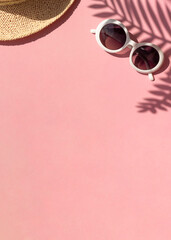 Stylish summer vacation concept frame with straw hat, retro sunglasses and tropical leaves shadows on the pink background. Copy space