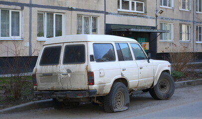 A large white SUV with a punctured wheel is parked in the courtyard of a residential building, Podvoysky Street, St. Petersburg, Russia, April 2022