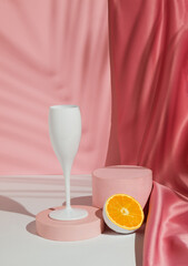 Wine glass with fresh orange fruit, tropical palm leaf shadow and podium on pastel pink background....