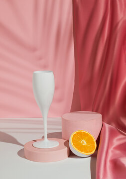 Wine glass with fresh orange fruit, tropical palm leaf shadow and podium on pastel pink background. Summer drink minimal concept. Suitable for Product Display.