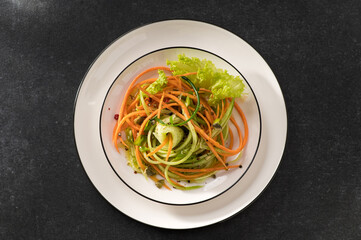fresh vegetable salad of carrots with cucumber on a white dish and gray background, top view, close-up