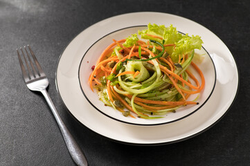 fresh vegetable salad of carrots with cucumber on a white dish and a gray background, serving, close-up
