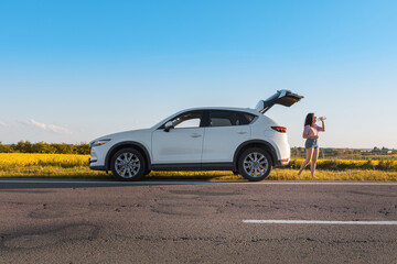 woman drinking water standing near car trunk on sunset at roadside