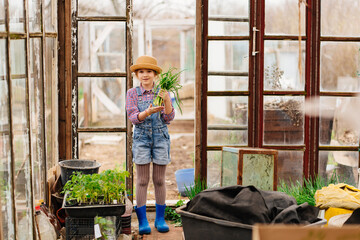 a funny little girl in a hat with green onions in the greenhouse 