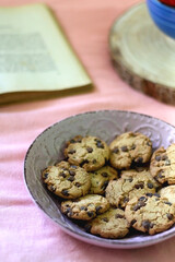Bowl of chocolate chip cookies, bowl of fresh strawberries, open book and reading glasses on the bed. Hygge at home. Selective focus.