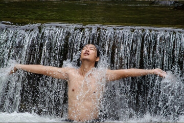 Asian man relaxing with freedom open arms in waterfall in tropical nature. Wellness spa concept in holiday nature.