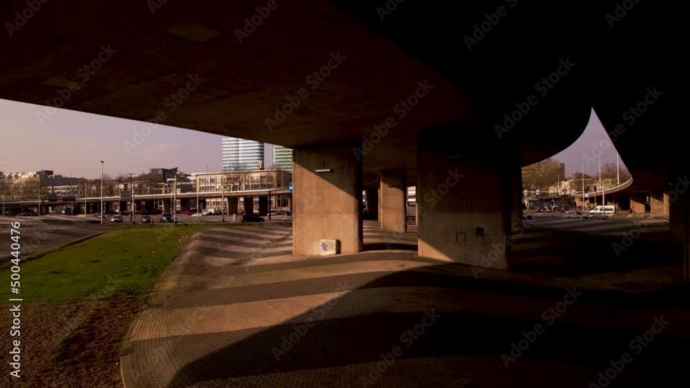 Poster aerial forwards movement through large concrete overpass columns of highway intersection in urban su