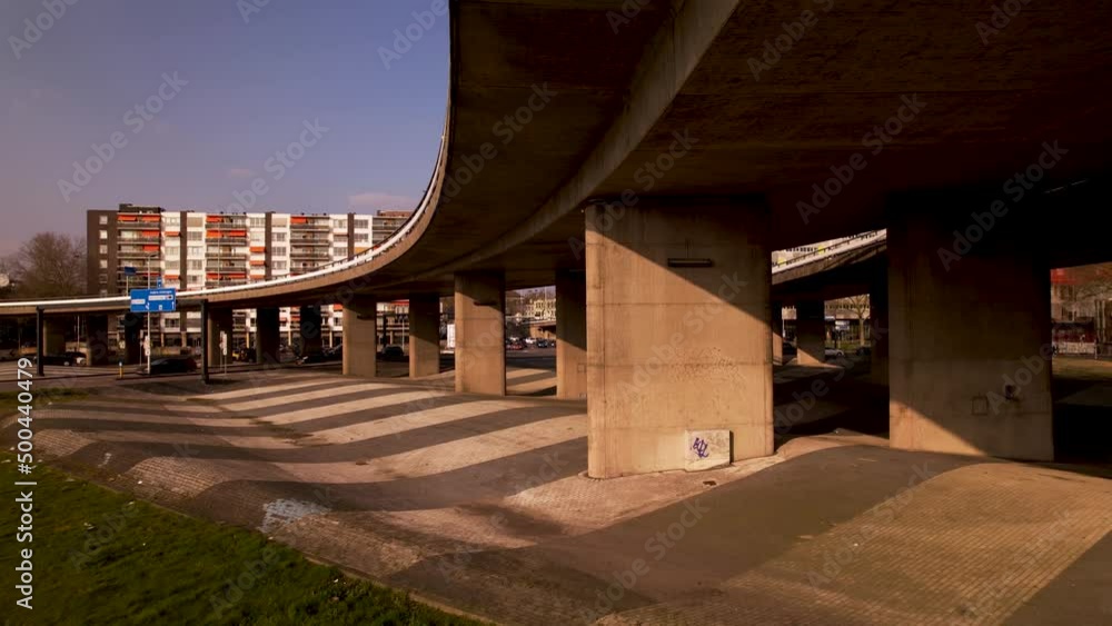 Poster aerial backwards reveal of wider city context around concrete overpass columns of highway intersecti