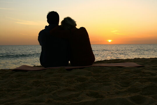 Deux amoureux sur une plage contemplant un magnifique coucher de soleil sur la mer