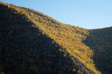 Game of shadow and light on a rocky mountain ridge covered by sunlit, autumn colored forests - 500441485