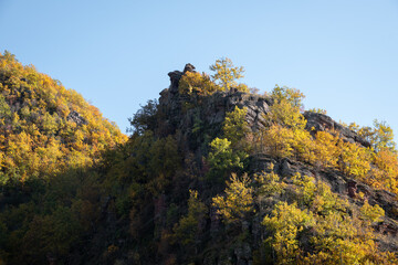 Impressive, pointy, rocky mountain peaks covered by autumn colored trees lighten by golden sun light - 500441494