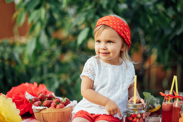 Lemonade Stand. Adorable little girl trying to sell lemonade. strawberry lemonade with ice and mint as summer refreshing drink in jars. Cold soft drinks with fruit. Child drinking smoothie in jar