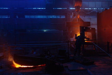 Worker operates metal casting process in metallurgical plant