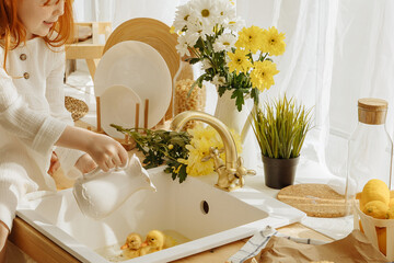 Little girl and cute ducklings are sitting in a basket in the kitchen.