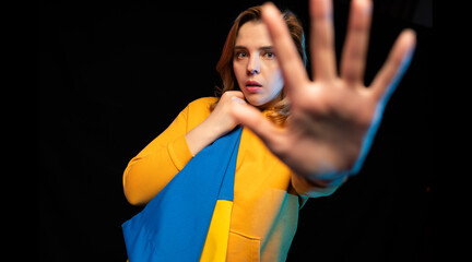 Beautiful Ukrainian girl with the national state flag of Ukraine on black background. Copy space. Russian Ukrainian War. Help and Pray for Ukraine. Stop war.