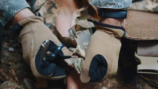 In forest military medic cuts the clothes of a wounded soldier with scissors to examine the body. Soldiers lying on ground. Blood around