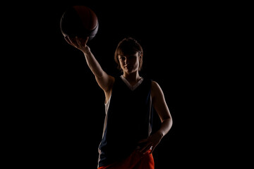 Female basketball player. Beautiful girl holding ball. Side lit silhouette studio portrait against black background