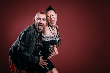 punky style man and woman pose in studio with cheerful expression on red background