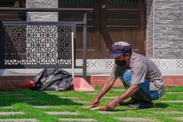 Asian worker is trimming grass on walkway in front yard area of office building