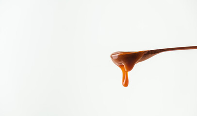 Salted caramel flows down the wooden spoon on the white background