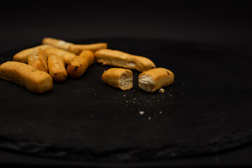 Grissini lying on a plate on a black background