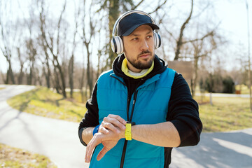 An athletic runner uses a smartwatch wireless headphones to monitor performance and listening music. Sportsman is happy with training progress.