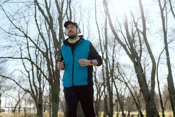 The concept of healthy living. An athletic man jogs through the park wearing wireless headphones and a wrist watch, the app counting calories burned, running route, heart rate, vital signs.