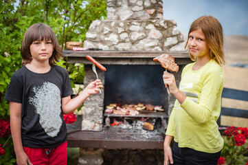 Children grilling meat. Boy and girl making barbecue in nature