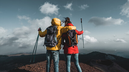 Back view of a couple of hikers with backpack and poles watching the panorama from the peak of...