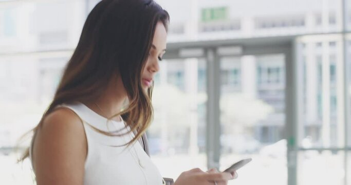 Im here to achieve all my greatest dreams. 4k video footage of a young businesswoman using a cellphone while walking in a modern office.