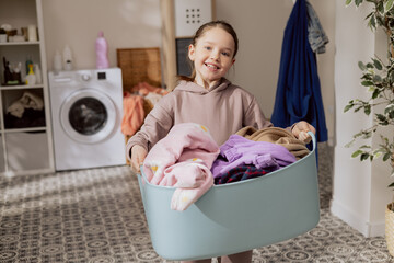 Smiling pretty girl stands in the middle of the bathroom, laundry room, holding a large bowl filled...