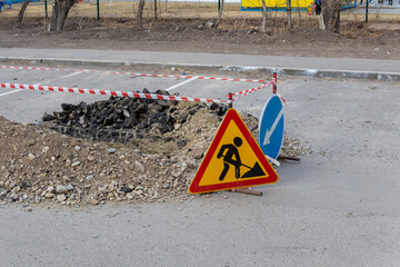 A trench dug in the middle of the road is fenced with road signs and protective tape. Repair of the...