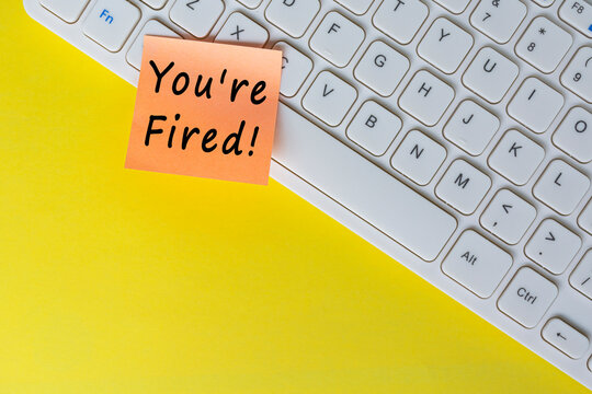 You're Fired text on orange sticky note on top of white keyboard.