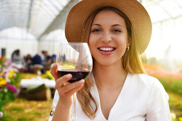 Photo of happy cheerful woman holds wine glass makes toast looking at camera isolated on greenhouse...