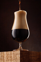 Glass of porter beer with overflowing foam head. Stream of dark stout pours into a beer glass