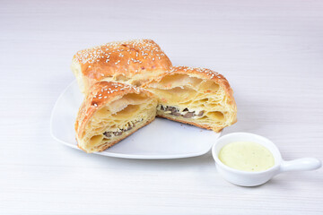 Puff pastry with mushrooms and cheese, sesame seeds and sauce on wooden background