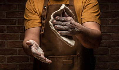 White flour flying into air as pastry chef in white suit slams ball dough on white powder covered...